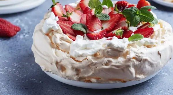 Puszysty tort bezowy z mascarpone i bitą śmietaną, ozdobiony świeżymi truskawkami i miętą.