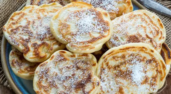 Puszyste racuchy na kefirze jak u babci, posypane cukrem pudrem, kuszą swoim domowym aromatem.