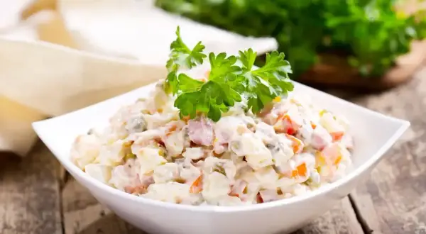 Sałatka jarzynowa w białej misce, udekorowana natką pietruszki. Zastanawiasz się, ile kcal ma sałatka jarzynowa?