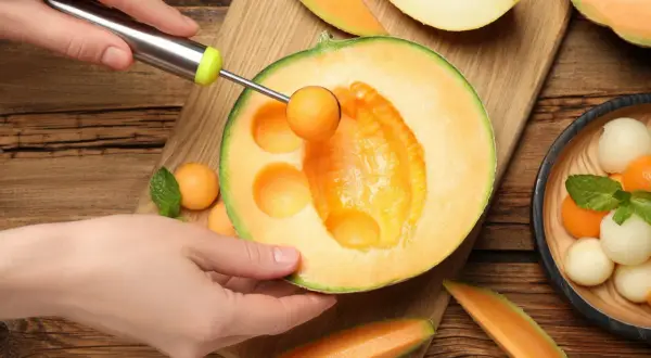 Ręka wydrąża kulki z melona, ukazując jego soczyste wnętrze. To dowód na bogactwo witamin i minerałów, czyli melon właściwości.