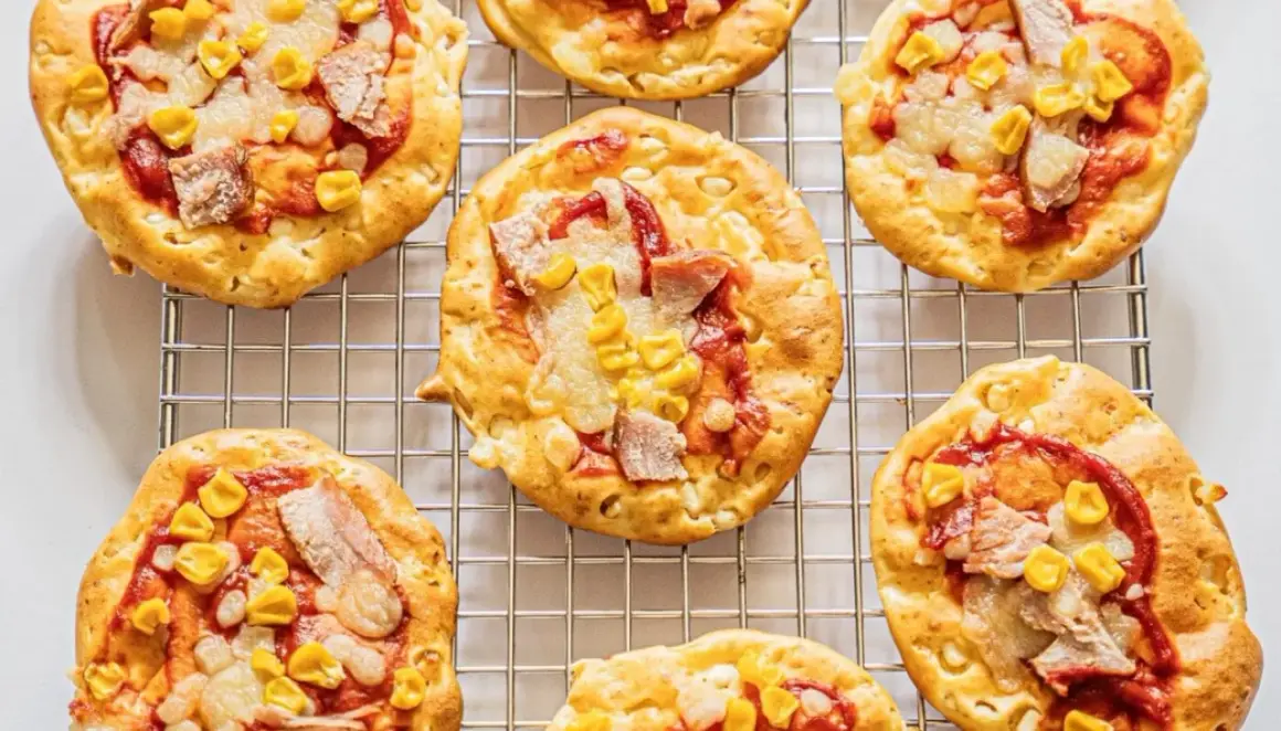 Mini pizze z serka wiejskiego, z kukurydzą i kawałkami mięsa, ułożone na metalowej kratce.