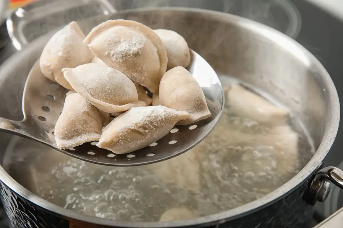 Gotowanie pierogów: na łyżce cedzakowej świeżo uformowane pierogi czekają na wrzucenie do wrzątku. W garnku bulgocze woda, gotowe do przyjęcia pysznego farszu.