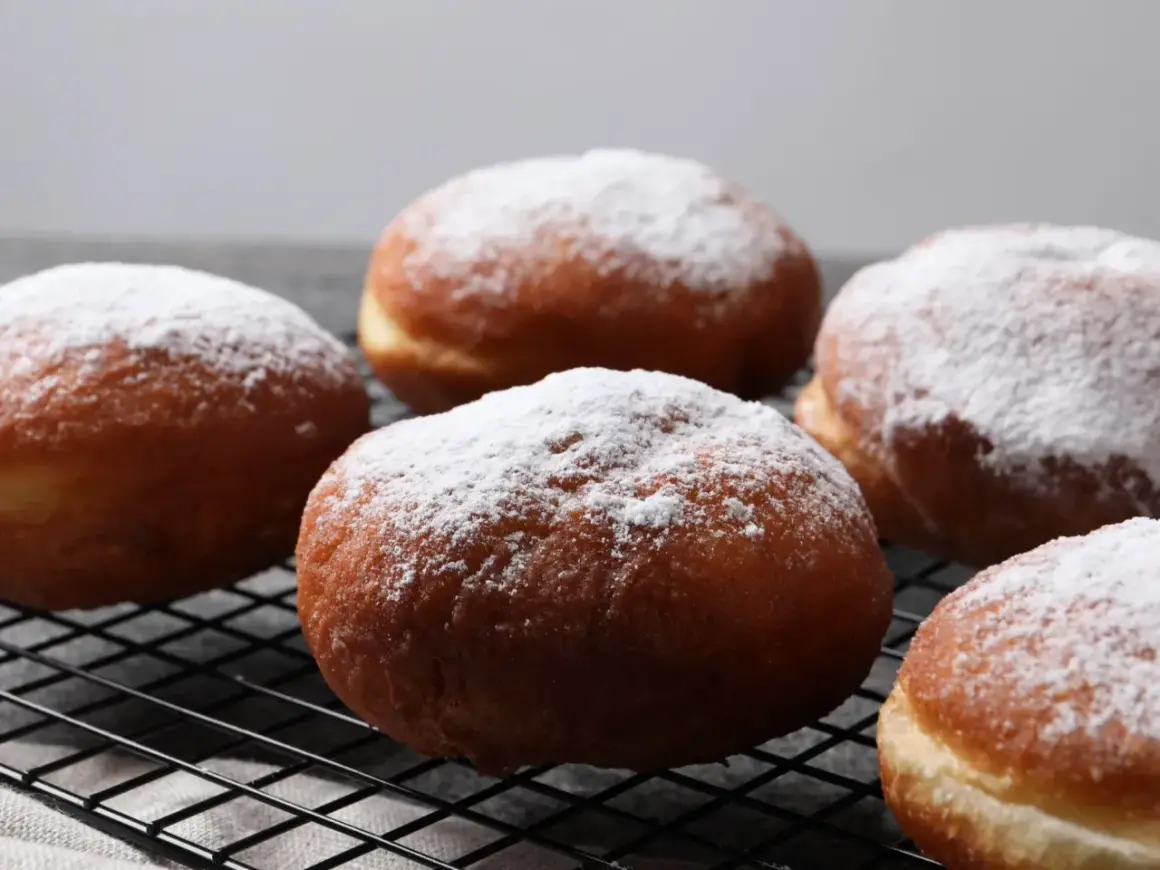 Szybkie pączki z piekarnika, oprószone cukrem pudrem, wyglądają apetycznie na czarnej kratce.
