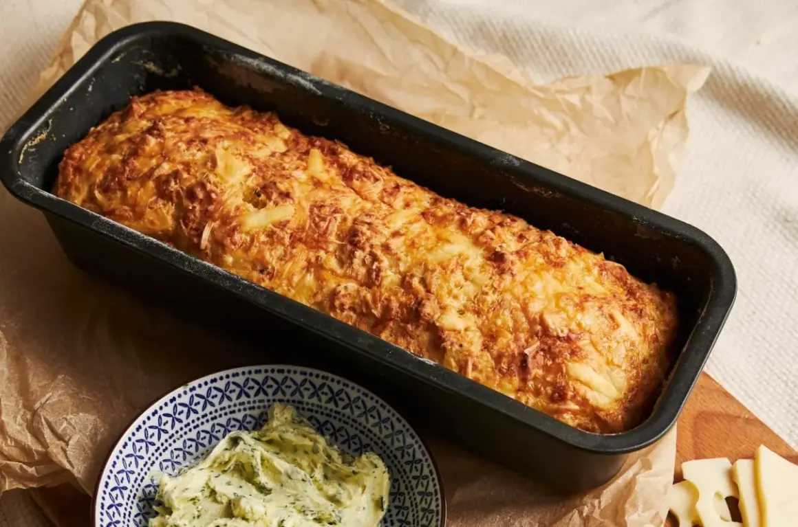 Chrupiąca babka ziemniaczana w keksówce, obok miseczka z masłem ziołowym.