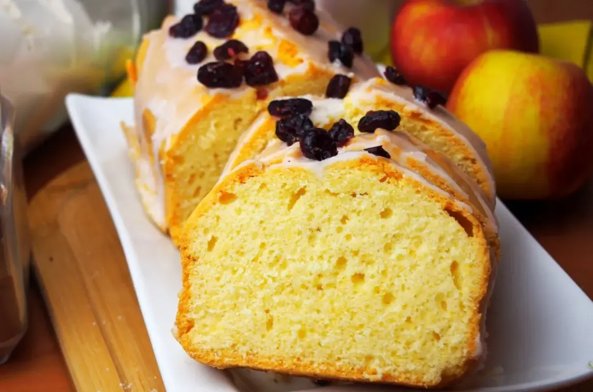 Pyszna, wilgotna babka cytrynowa z lukrem i żurawiną, obok jabłka.
