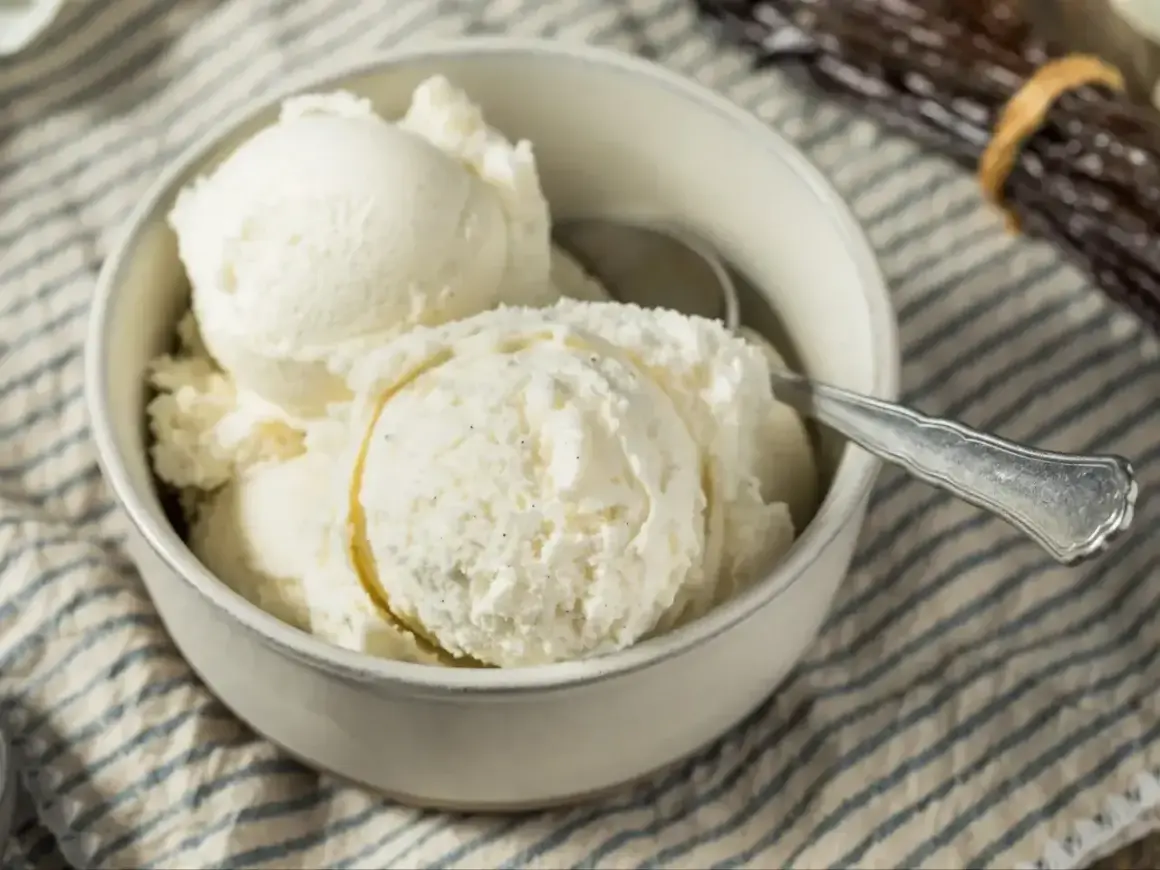 Puszyste lody z mascarpone w miseczce, gotowe do schrupania. Obok leżą laski wanilii.