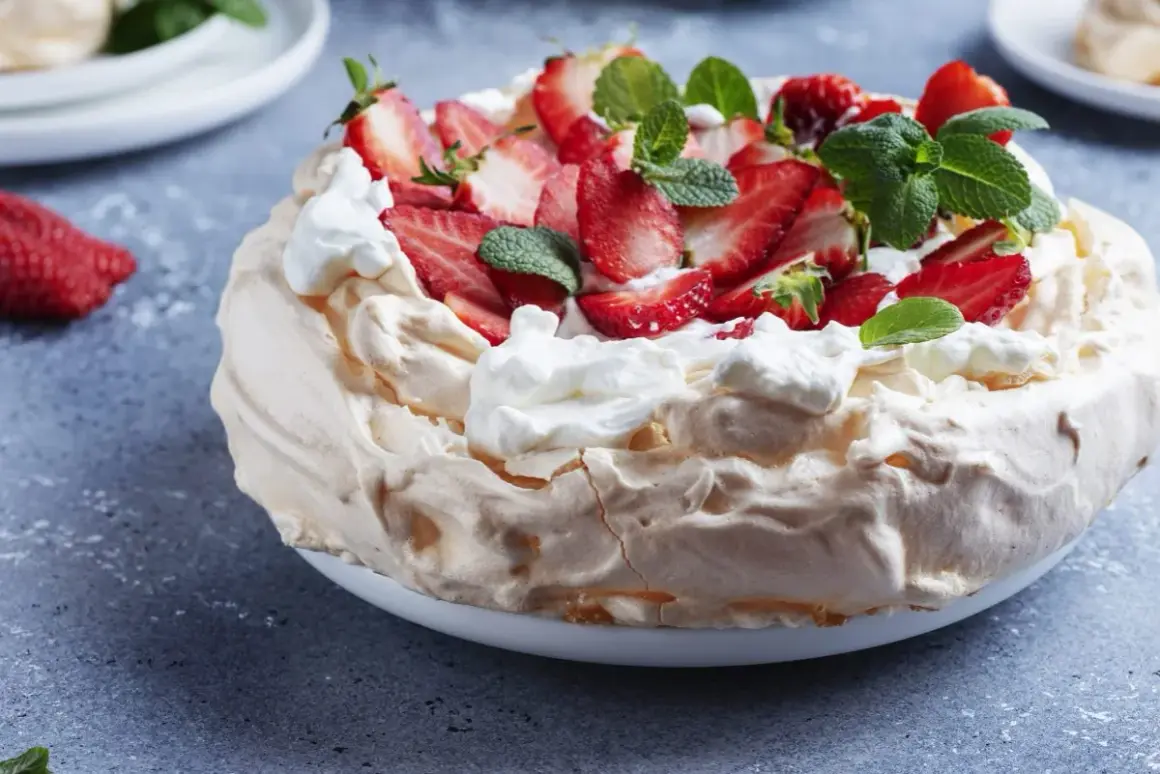 Puszysty tort bezowy z mascarpone i bitą śmietaną, ozdobiony świeżymi truskawkami i miętą.