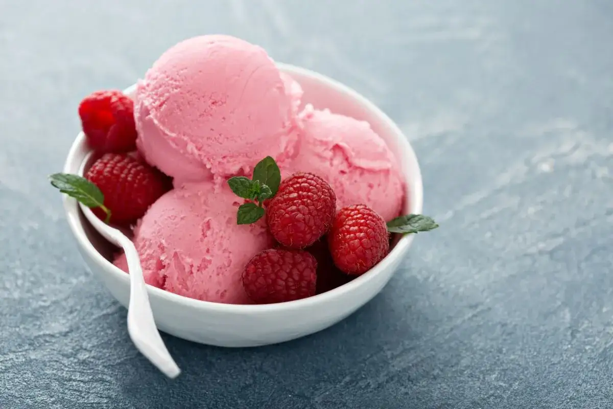 Pyszne lody z mascarpone, malinami i listkami mięty w białej miseczce. Idealny deser na upalne dni.
