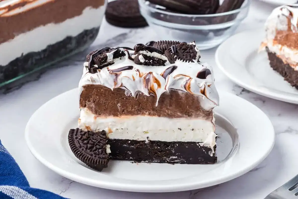 Warstwowy deser z kremem czekoladowym, śmietankowym i pokruszonymi oreo. Na wierzchu bita śmietana i polewa czekoladowa.