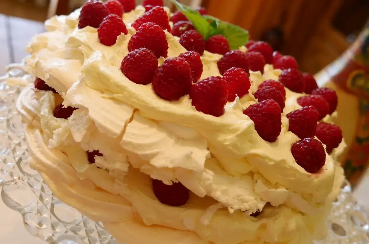 Pyszny tort bezowy z mascarpone i bitą śmietaną, ozdobiony malinami. Idealny na każdą okazję.