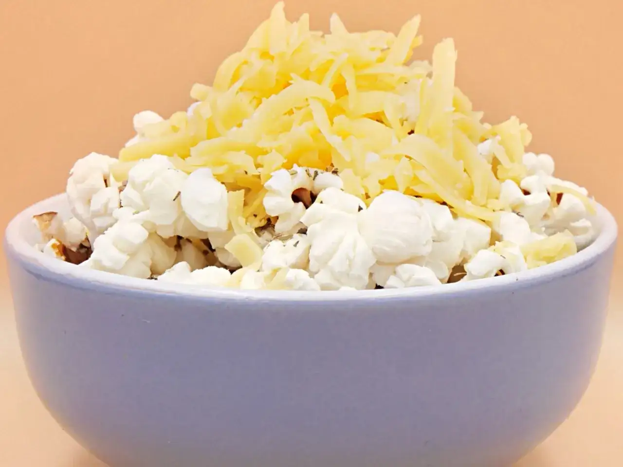 Miseczka popcornu posypana startym żółtym serem. Pyszna przekąska, ale warto pamiętać o jej popcorn kcal.
