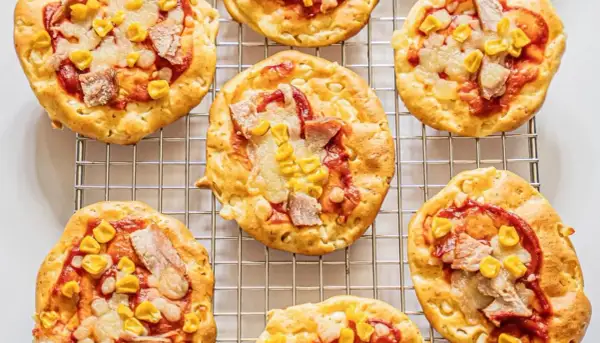 Mini pizze z serka wiejskiego, z kukurydzą i kawałkami mięsa, ułożone na metalowej kratce.