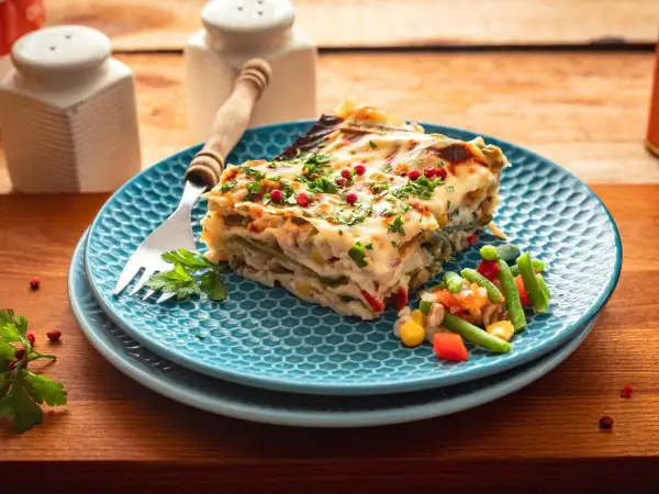 Kawałek pysznej, warzywnej lasagne na niebieskim talerzu, posypany natką i pieprzem. To bardzo dobry przepis na lazanię, który zachwyci każdego!