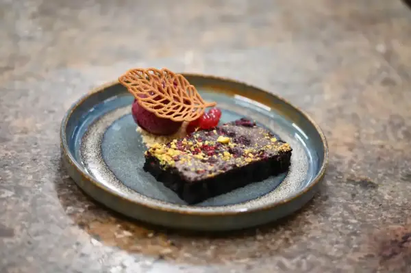 Elegancka monoporcja: czekoladowy brownie z malinami, sorbetem malinowym i dekoracją z listka.