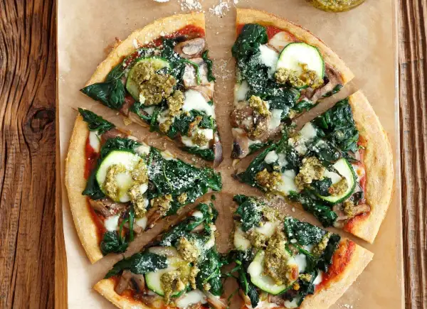 Pyszna pizza ze szpinakiem, cukinią i grzybami, polana zielonym pesto.