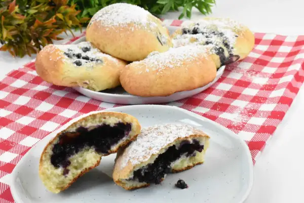 Pyszne, domowe jagodzianki posypane cukrem pudrem, jedna przekrojona, ukazująca soczyste nadzienie.