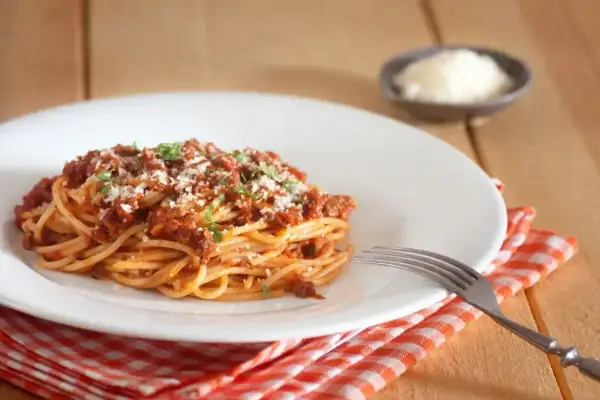 Porcja spaghetti bolognese, posypana parmezanem i natką pietruszki. Idealne na obiad, z uwzględnieniem spaghetti bolognese kcal.