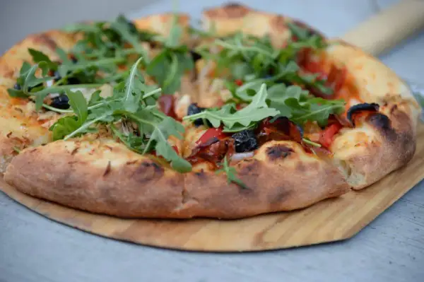 Pyszne, świeżo upieczone ciasto na pizzę z rukolą, oliwkami i papryką, podane na drewnianej desce.