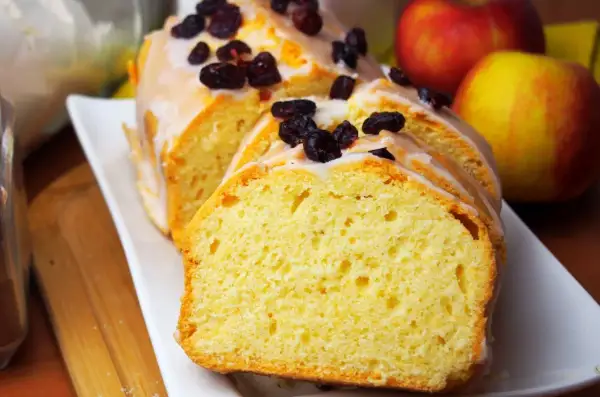 Pyszna, wilgotna babka cytrynowa z lukrem i żurawiną, obok jabłka.