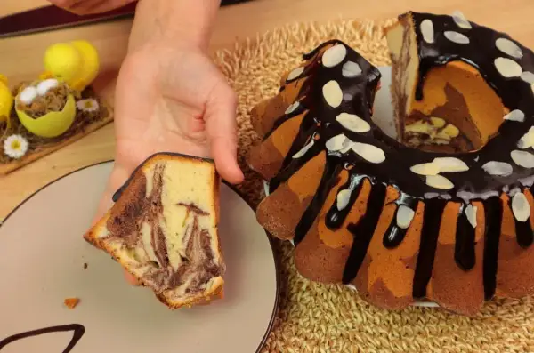 Najbardziej wilgotna babka w paski, polana czekoladą i posypana płatkami migdałów, z kawałkiem na talerzu.
