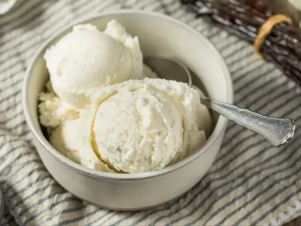 Puszyste lody z mascarpone w miseczce, gotowe do schrupania. Obok leżą laski wanilii.
