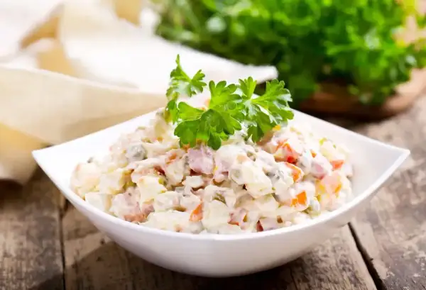 Sałatka jarzynowa w białej misce, udekorowana natką pietruszki. Zastanawiasz się, ile kcal ma sałatka jarzynowa?