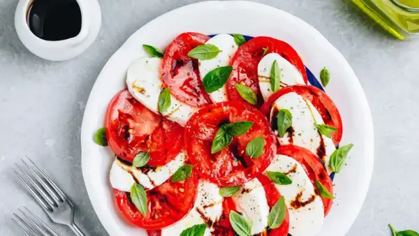 Sałatka caprese: plastry soczystego pomidora z mozzarellą, skropione balsamico i udekorowane listkami bazylii.