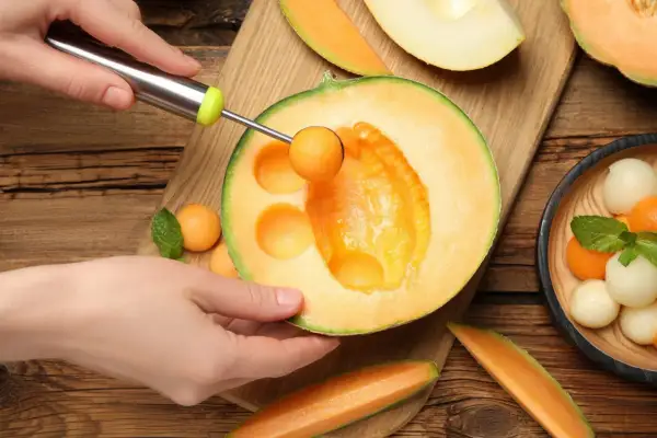 Ręka wydrąża kulki z melona, ukazując jego soczyste wnętrze. To dowód na bogactwo witamin i minerałów, czyli melon właściwości.