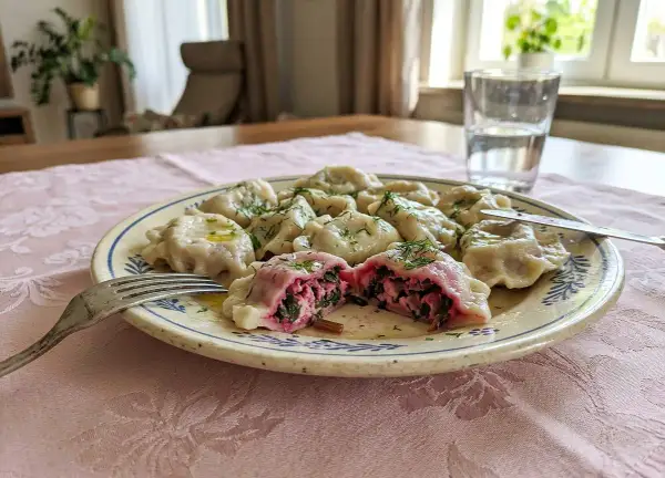 Pyszne pierogi z farszem na pierogi ruskie Magdy Gessler, polane masłem i posypane koperkiem. Jedna pierożka przekrojona, ukazująca bogate wnętrze.